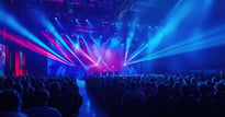 A large audience watches a stage show, illuminated by vibrant blue and red lights