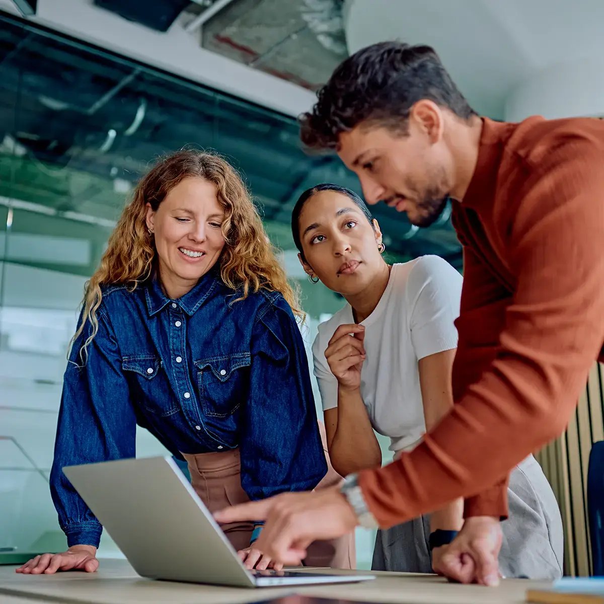 A diverse team in a modern office engages with a laptop, displaying focus and collaboration