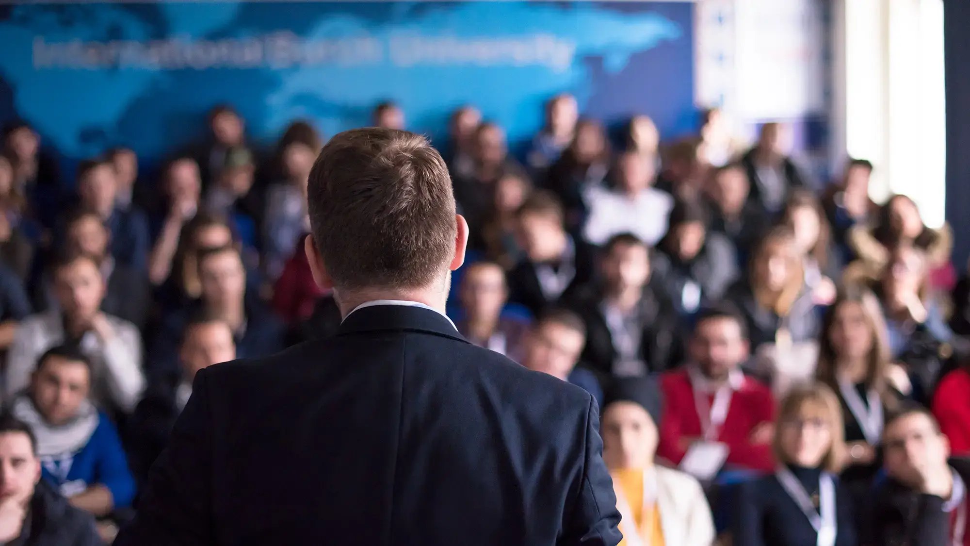 A man in a suit is speaking to a focused audience in a university lecture hall