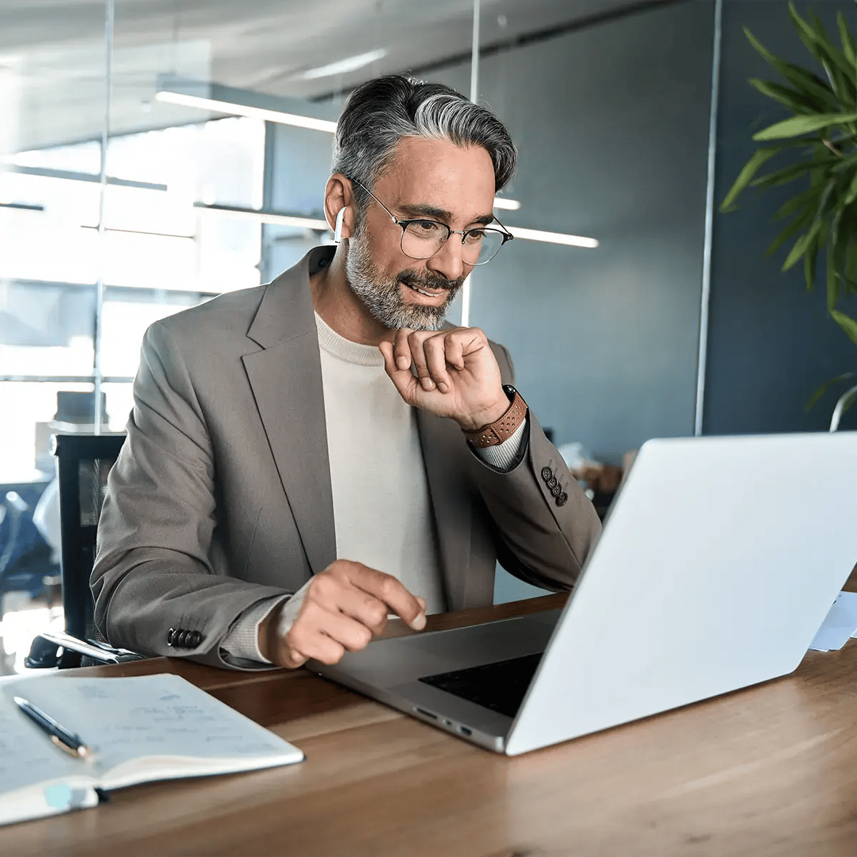 Smiling man with glasses and gray hair using a laptop in an office