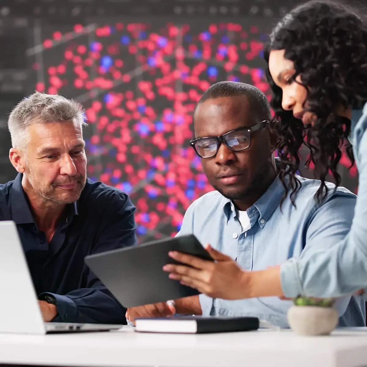 Three colleagues collaborate, examining a digital tablet in a modern office