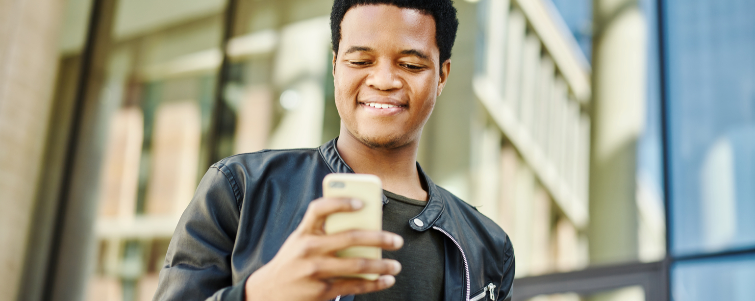 Portrait of handsome black man in leather jacket using cell phone on the move and smiling