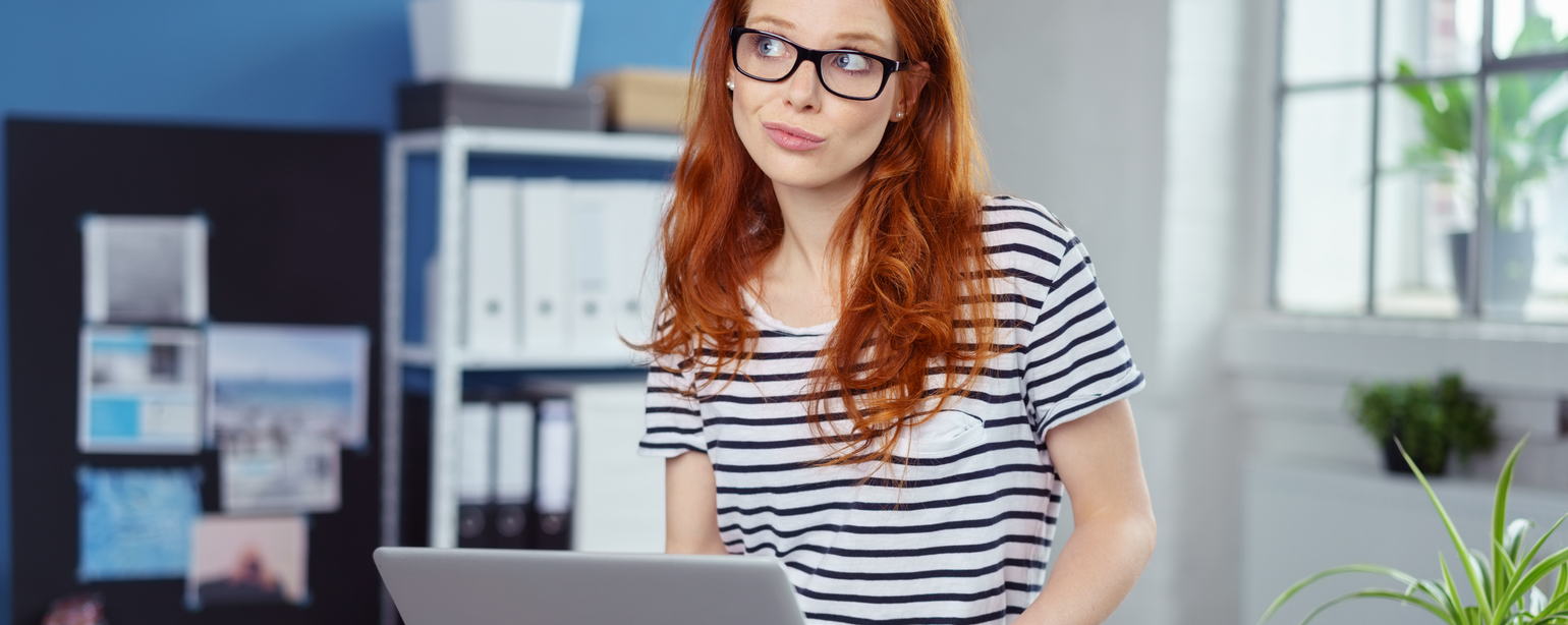 Thoughtful charismatic young redhead woman using a laptop balanced on her lap fb