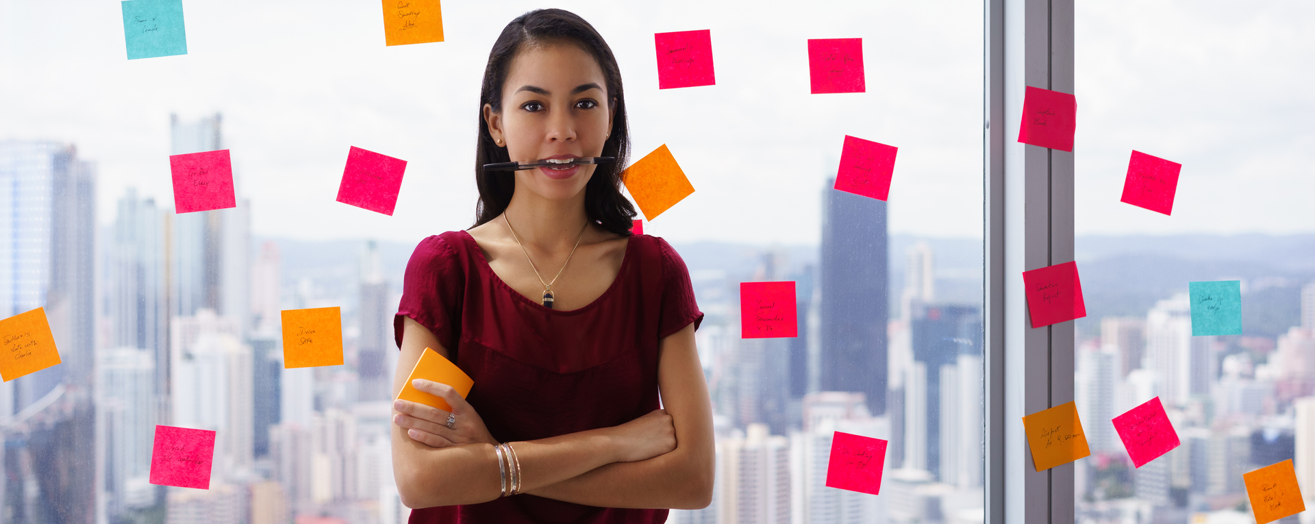 woman stands in office at high floor, against window full of adhesive notes with tasks