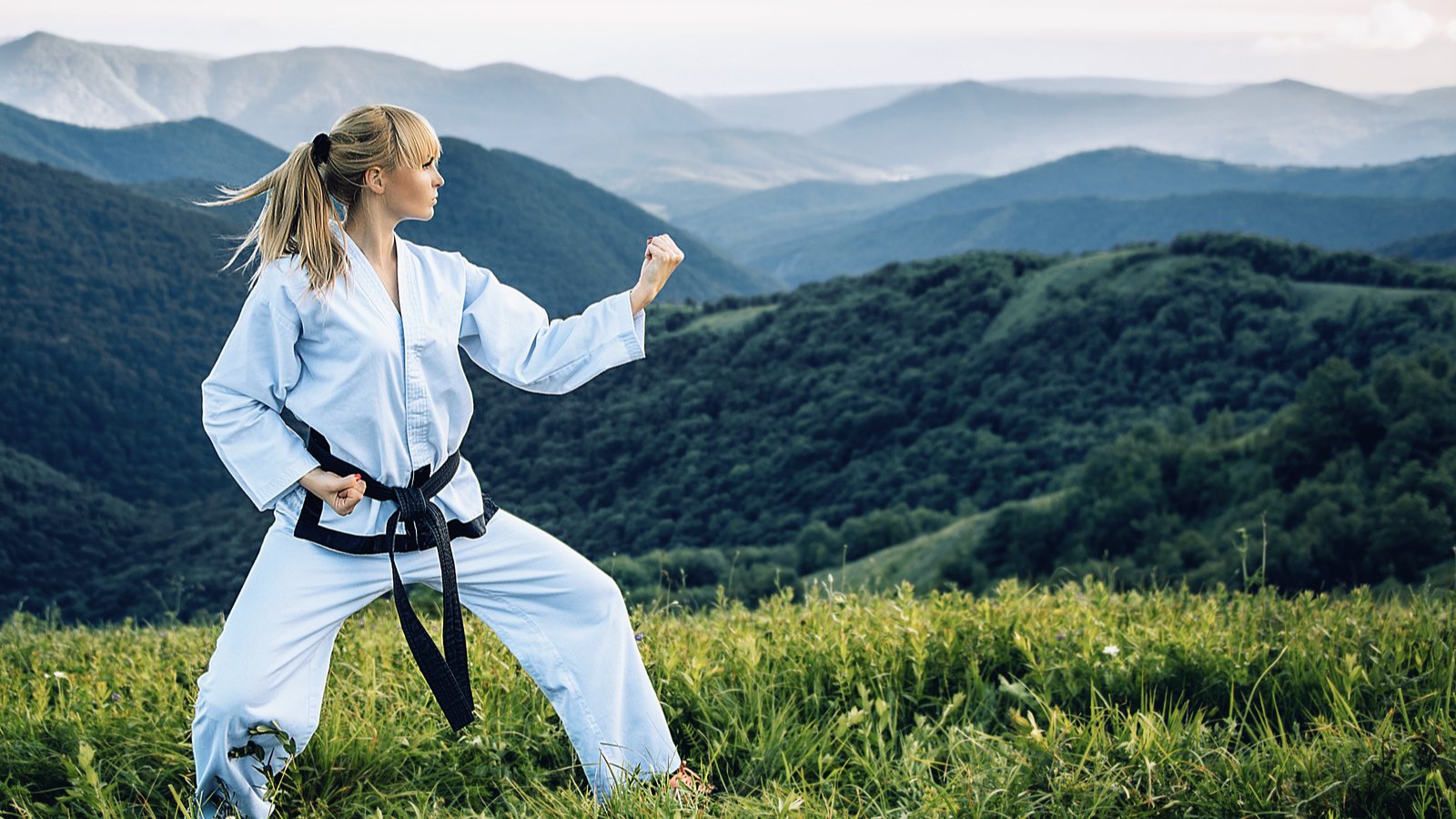A young lady with a black belt coaches in martial art outdoors