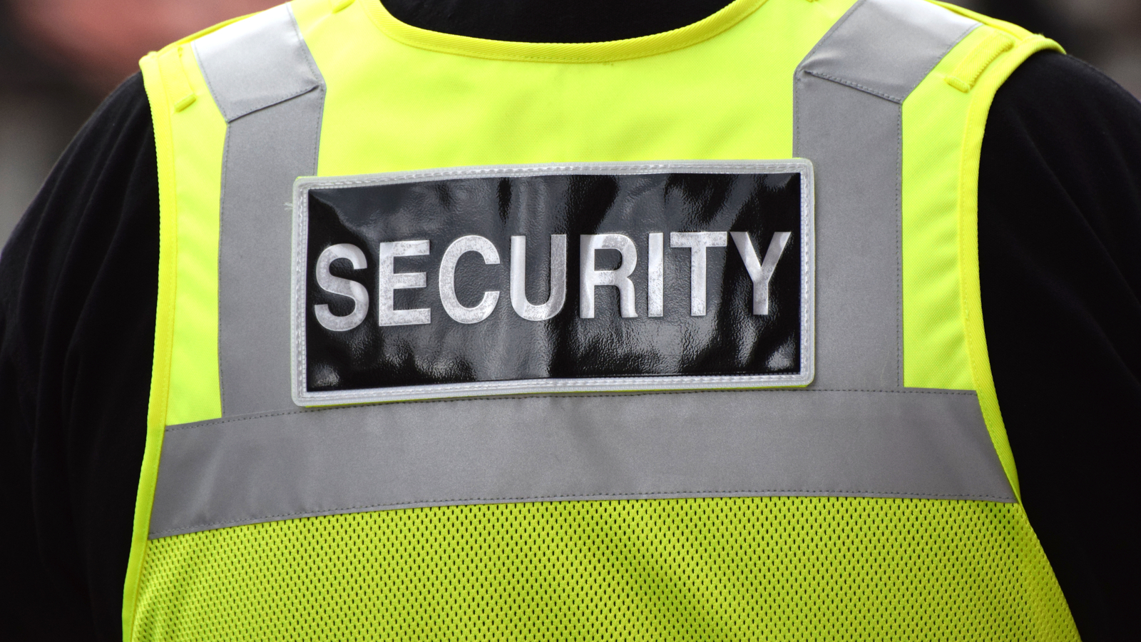 Close up of the word security written on the back of a security guards yellow vest