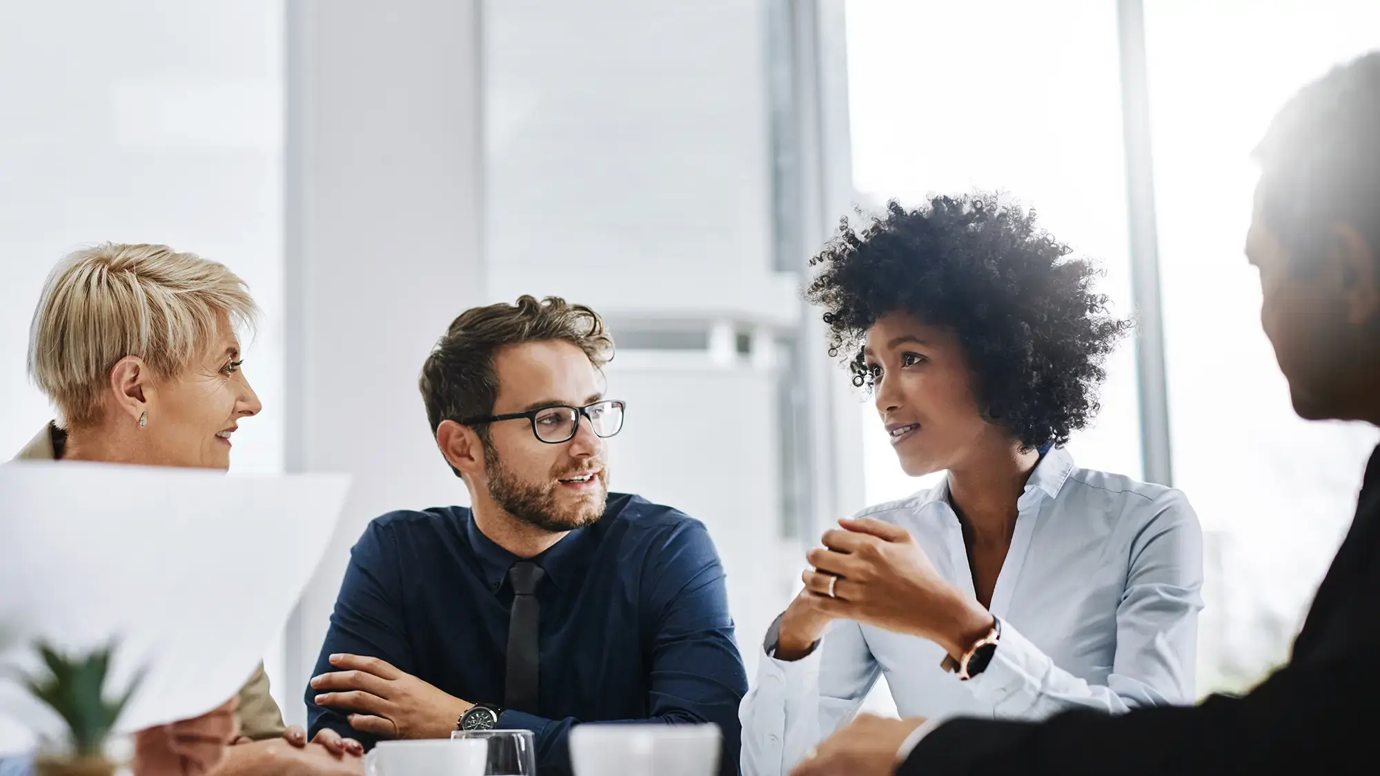 A diverse group of four people is having a focused discussion in a bright office setting