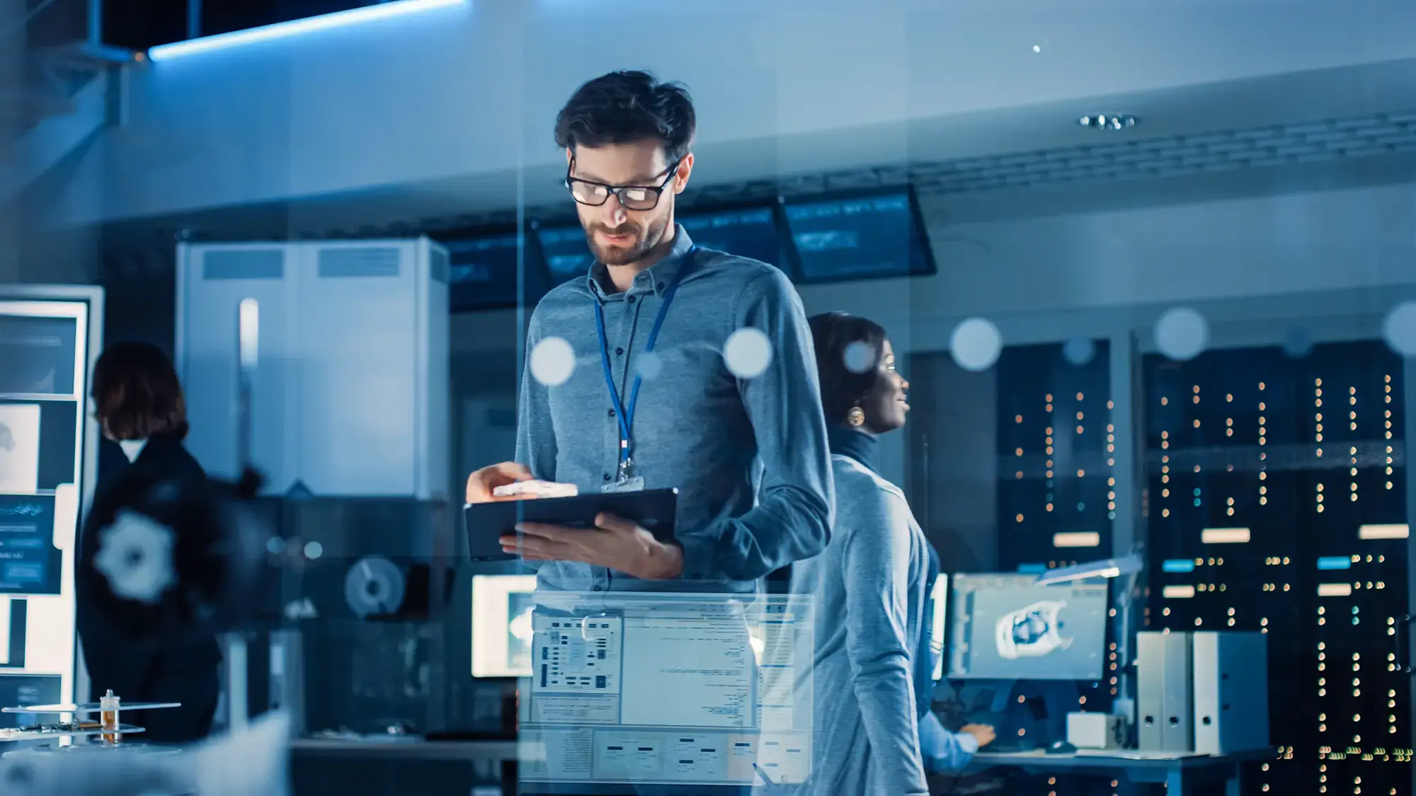 A man in a tech lab stands focused, holding a tablet