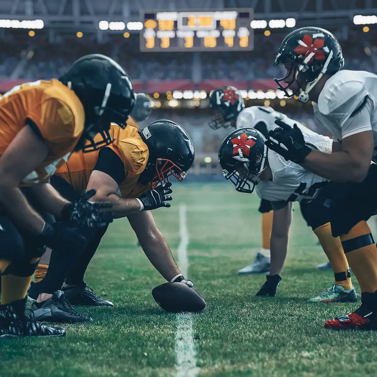 Football players in orange and white jerseys face off at the line of scrimmage on a vibrant green field