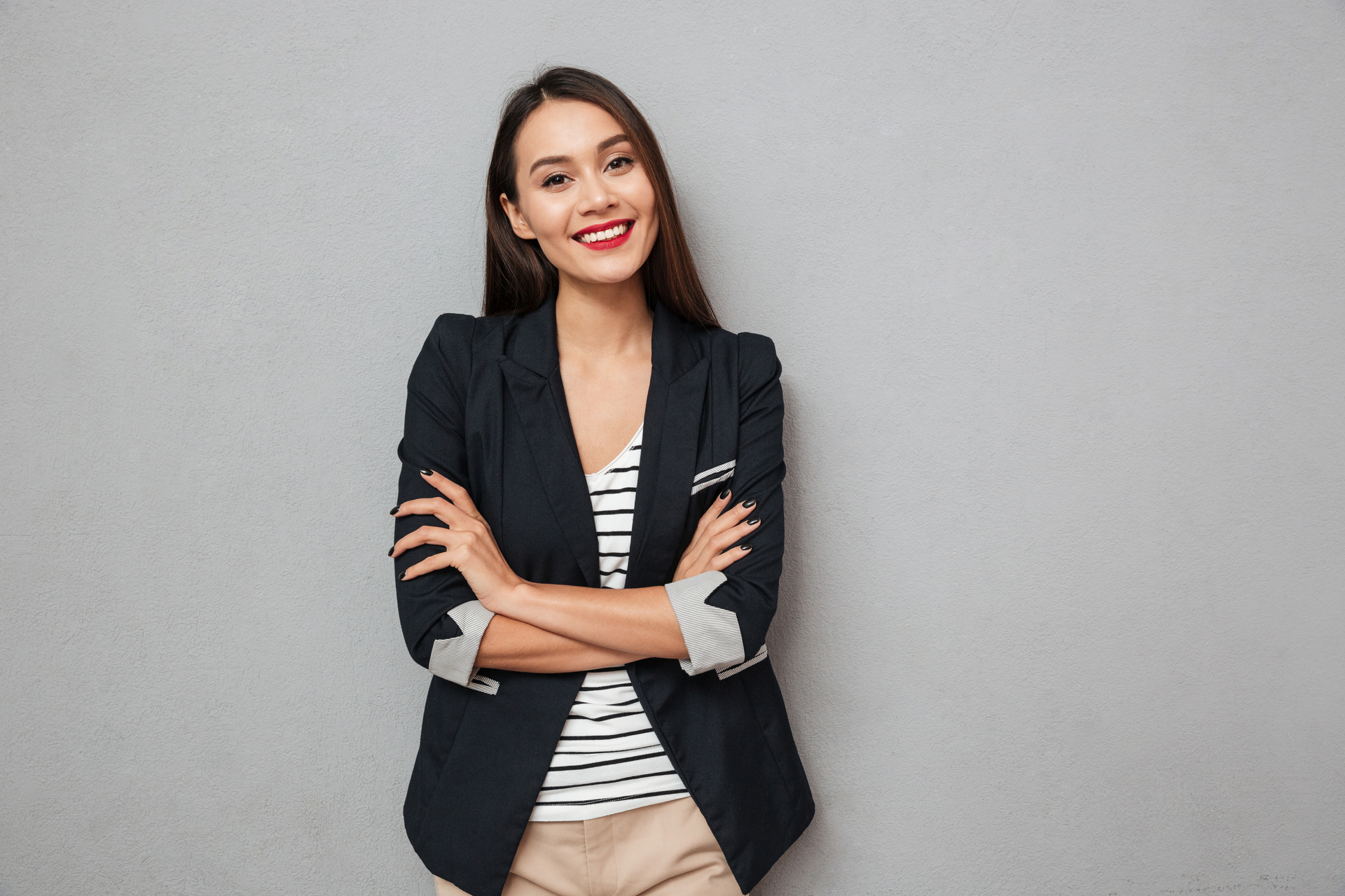 Pleased Asian business woman with crossed arms looking at the camera over gray background