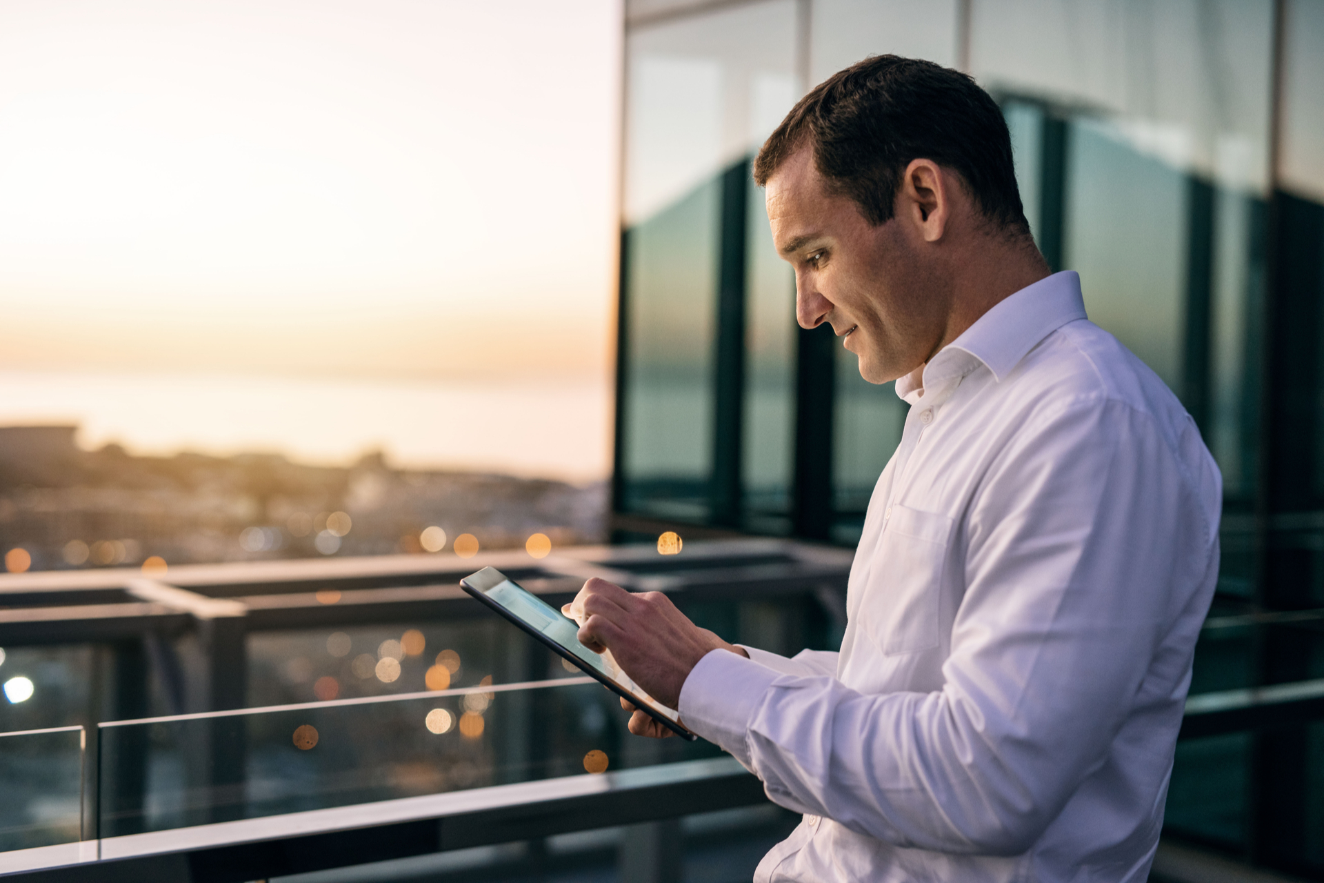 Smiling mature businessman working online with a digital tablet while standing outside on an office building balcony