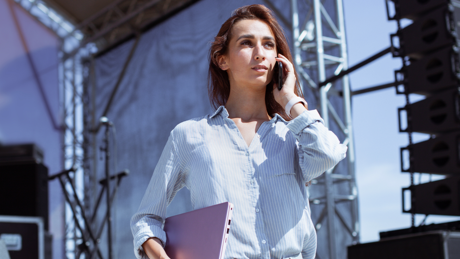 You woman standing in front of a stage speaking on a phone at a open air live event feature