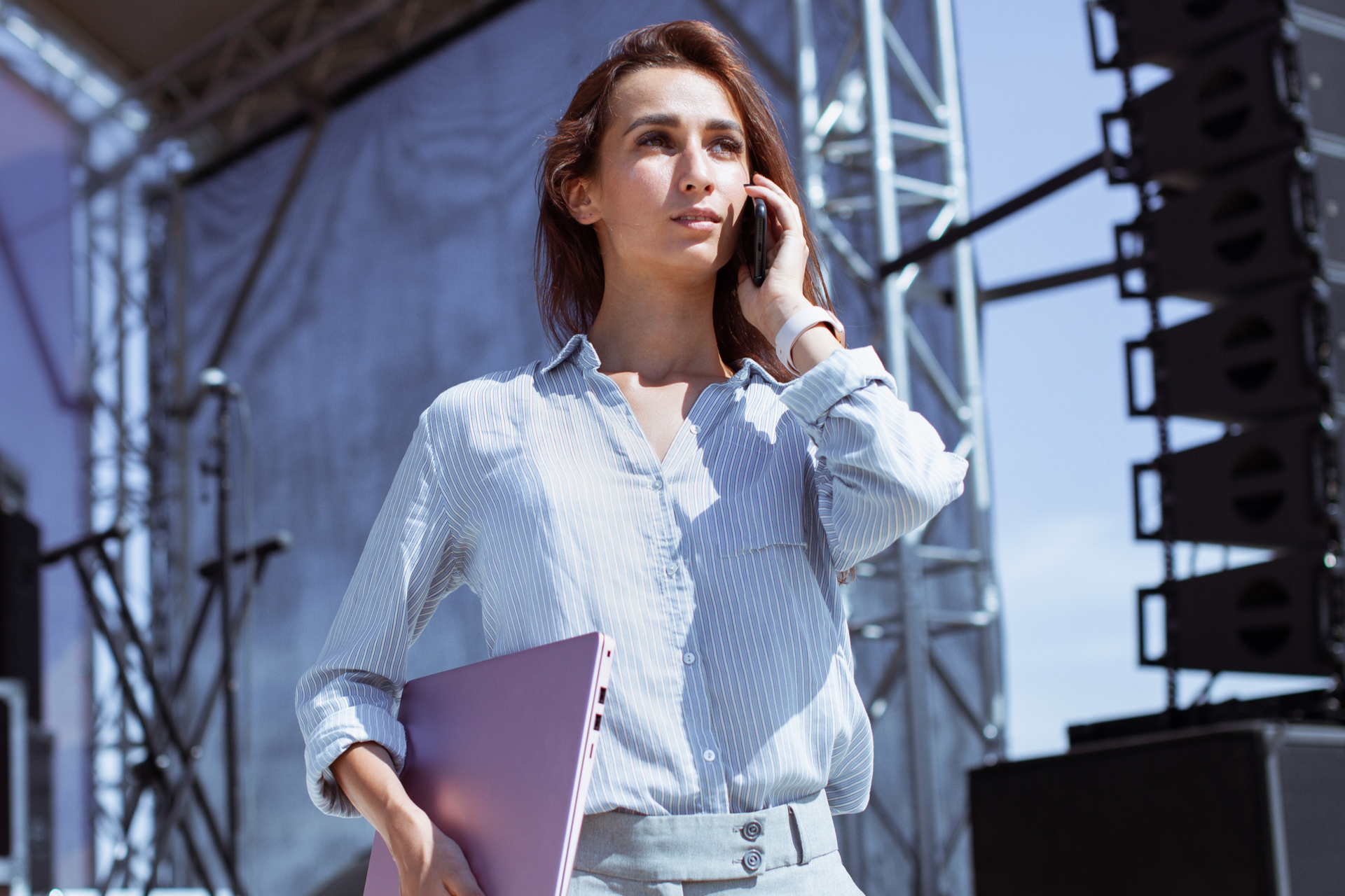 You woman standing in front of a stage speaking on a phone at a open air live event