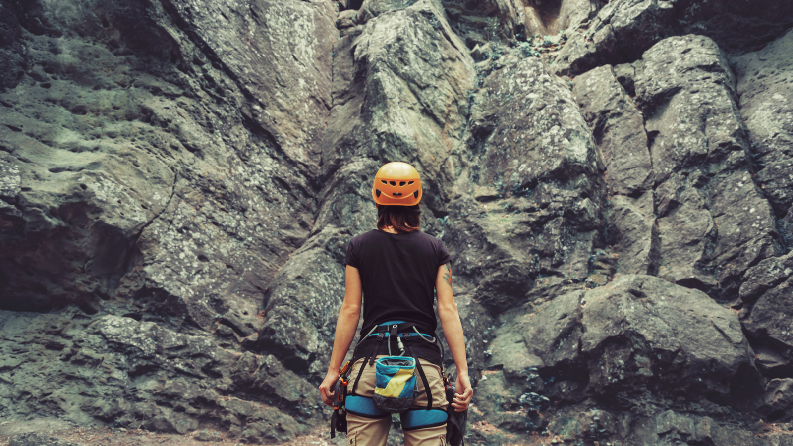 Young woman wearing in climbing equipment standing in front of a stone rock