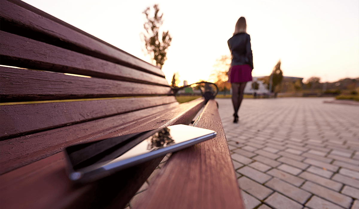 Woman walking away as she accidentally leaves her cell phone on a park bench